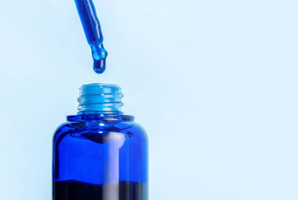 Blue liquid dropper above glass bottle